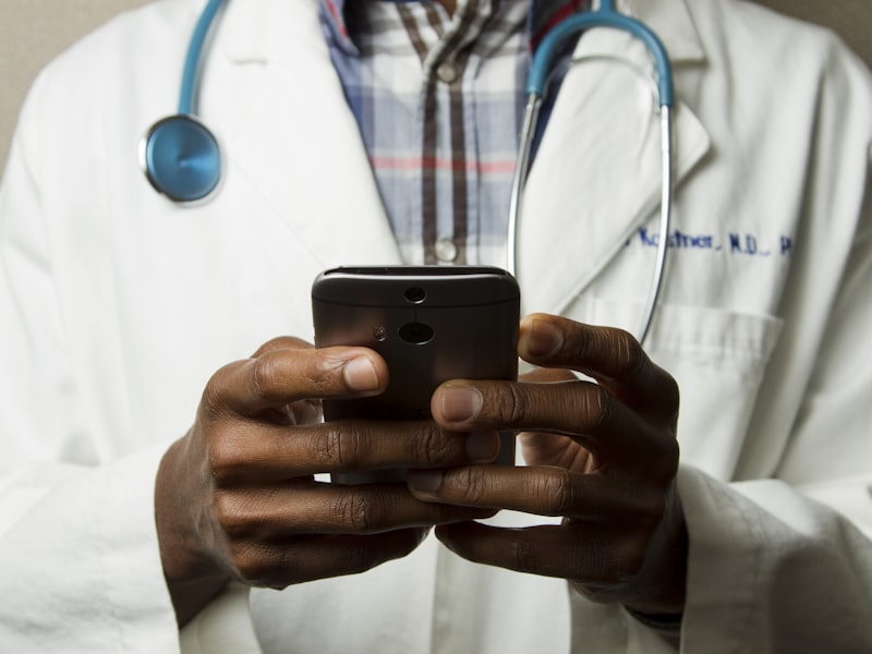 Medico in camice bianco con stetoscopio che utilizza uno smartphone